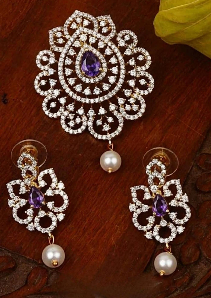 Elegant zircon diamond gold plated pendant set featuring a floral-inspired pendant designed with sparkling white zircon stones arranged in circular patterns. The centerpiece showcases a pear-shaped emerald violet stone surrounded by dazzling zircon stones, finished with a delicate pearl drop. The matching earrings mirror the same floral design with green stone and pearl danglers, Perfect for weddings, festivals, office wear, functions and its anti fade color