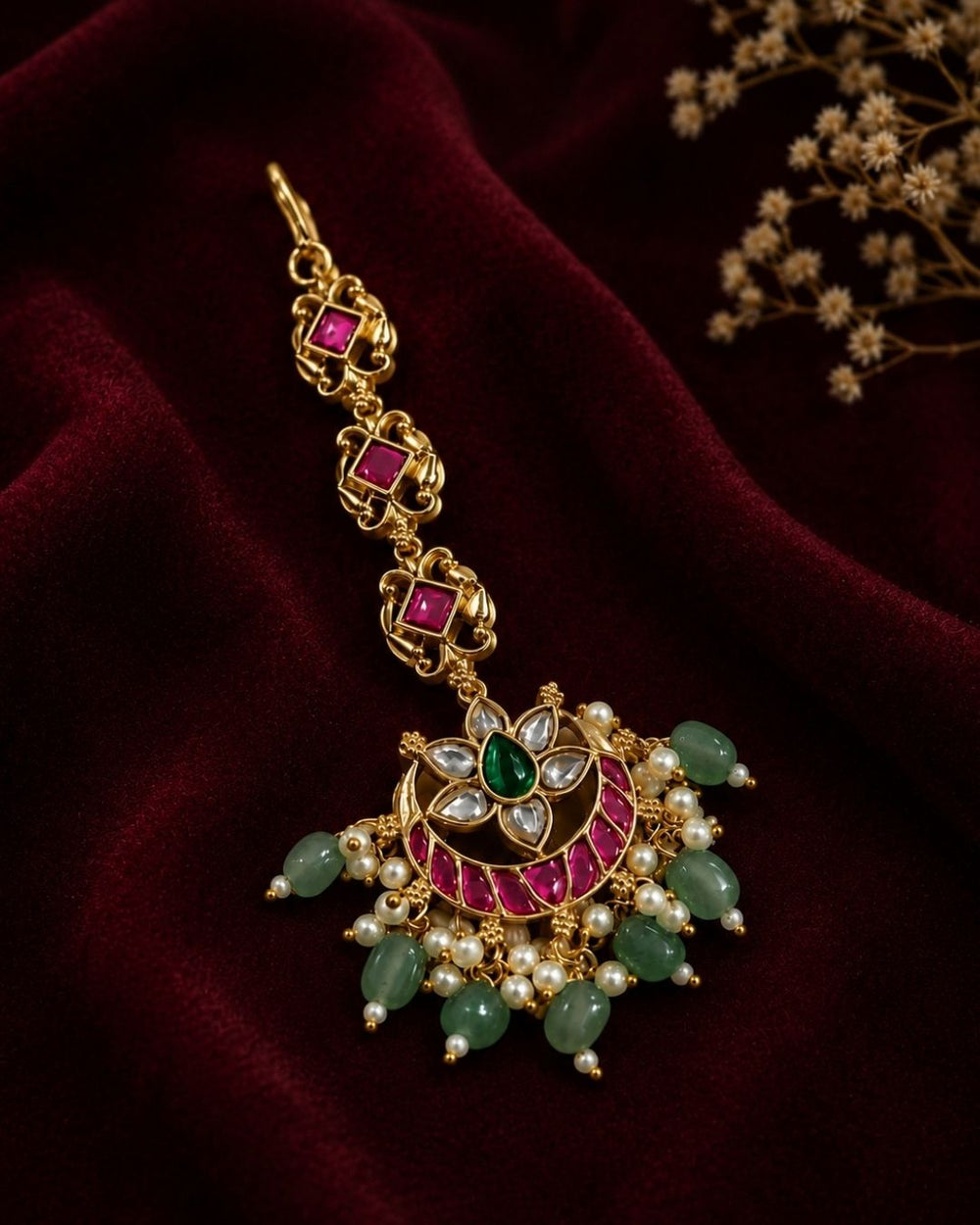 Beautiful traditional gold plated maang tikka featuring a pink stone chain, a floral-inspired circular pendant with green and pink stones, sparkling white accents, clusters of pearls, and multiple green bead drops. Perfect for weddings, festive occasions, traditional outfits, bridal styling, and special celebrations.