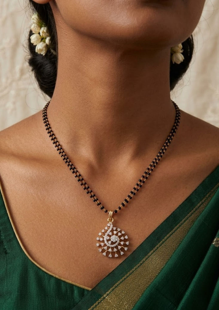 Close up of women wearing a gold plated bridal mangalsutra combo set. The main double-strand black bead necklace features an openwork swirling teardrop pendant densely paved with pure Zirconian diamonds. The matching set includes a pair of teardrop earrings, a coordinate statement ring, an adjustable sliding leaf bracelet, and a rigid round bangle.