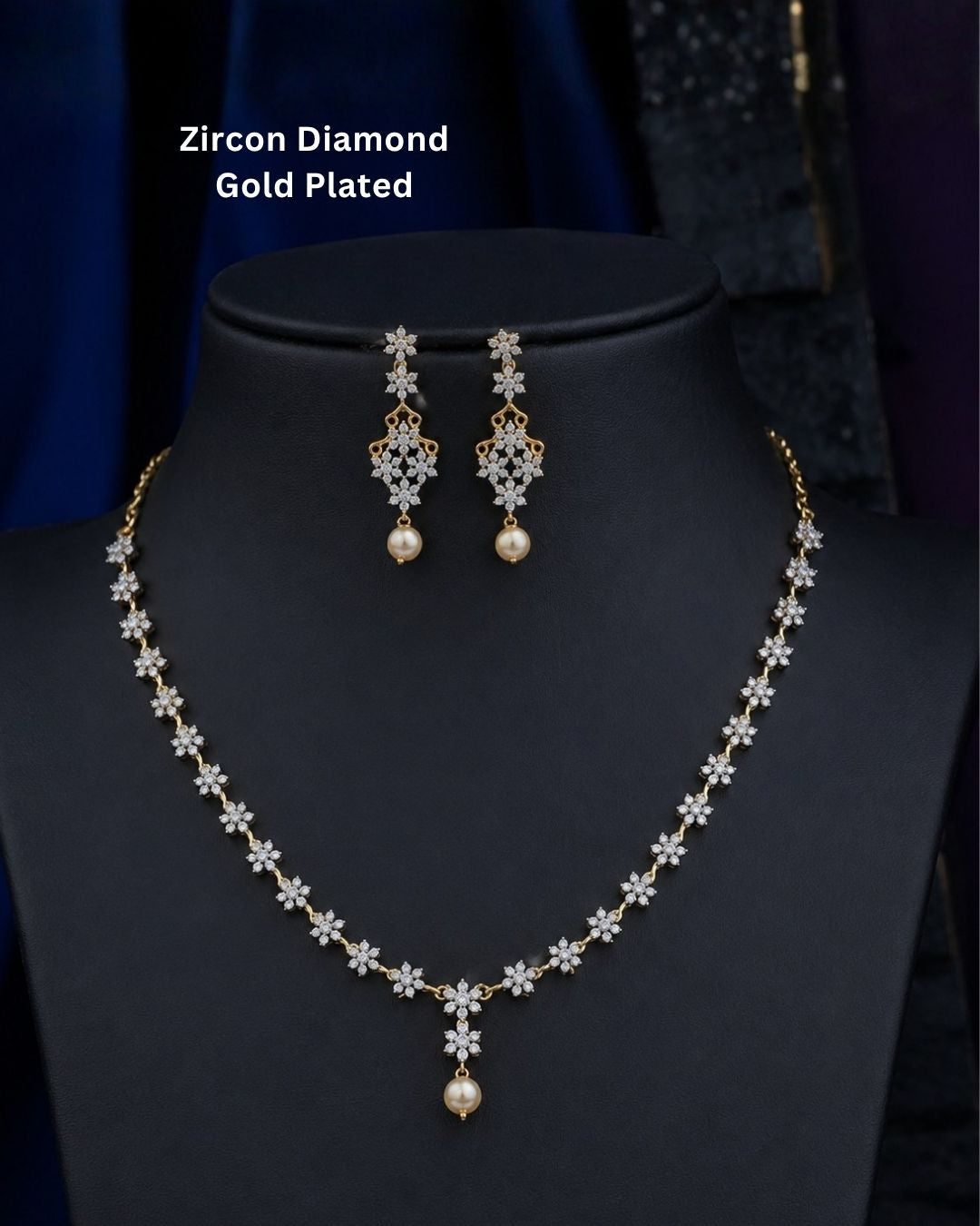 Gold plated diamond replica necklace set featuring delicate floral motifs, sparkling stones, and matching drop earrings with pearl accents, displayed on a maroon jewellery bust.
