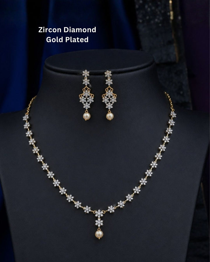 Gold plated diamond replica necklace set featuring delicate floral motifs, sparkling stones, and matching drop earrings with pearl accents, displayed on a maroon jewellery bust.
