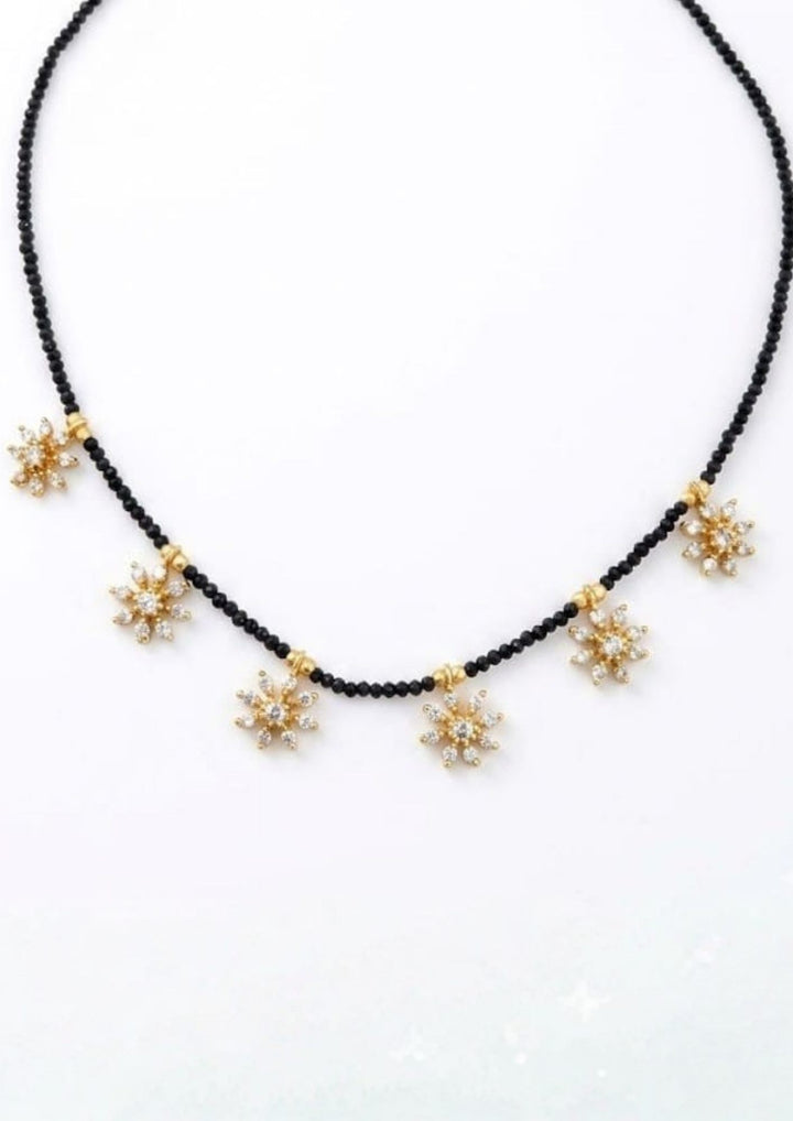 Gold plated mangalsutra delicate design with black beads and diamond flowers on white background flat lay detail for pooja, south indian festivals