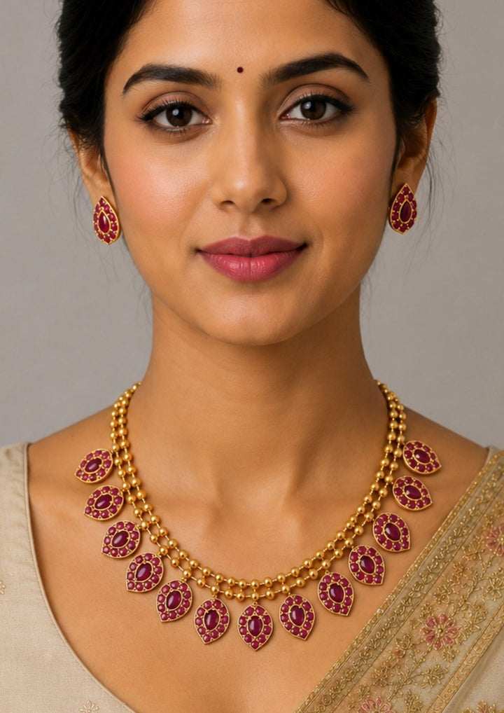 Woman wearing a gold necklace with red gemstones 