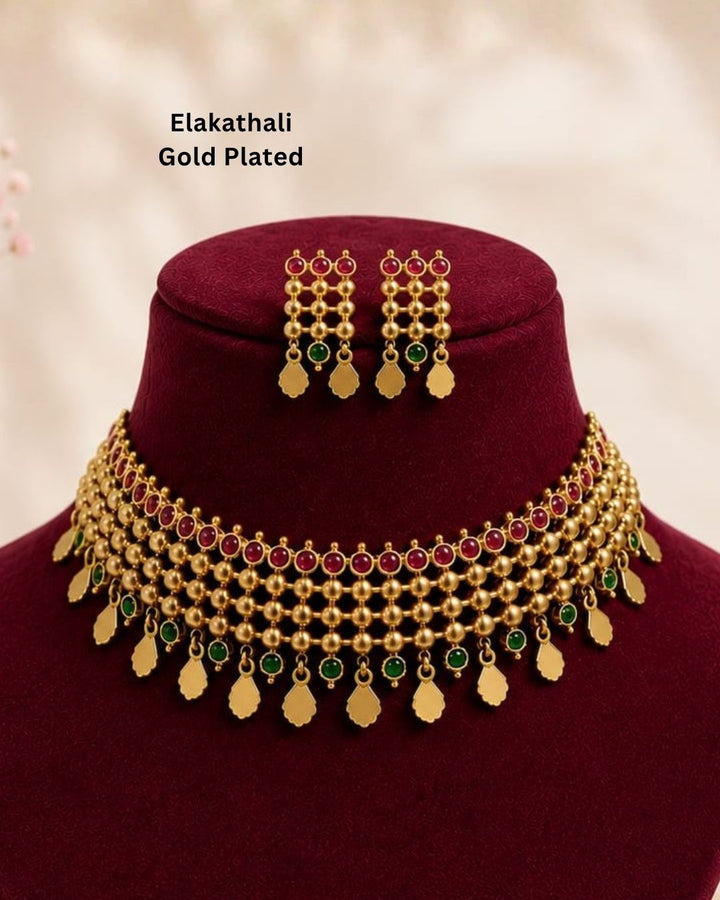 South Indaian women Beautiful Jadau Kundan gold plated necklace set featuring an intricate multi-layered choker design with ruby and green stones, detailed gold beadwork, dangling motifs, and matching earrings. Perfect for festive occasions, traditional wear, weddings, and gifting.