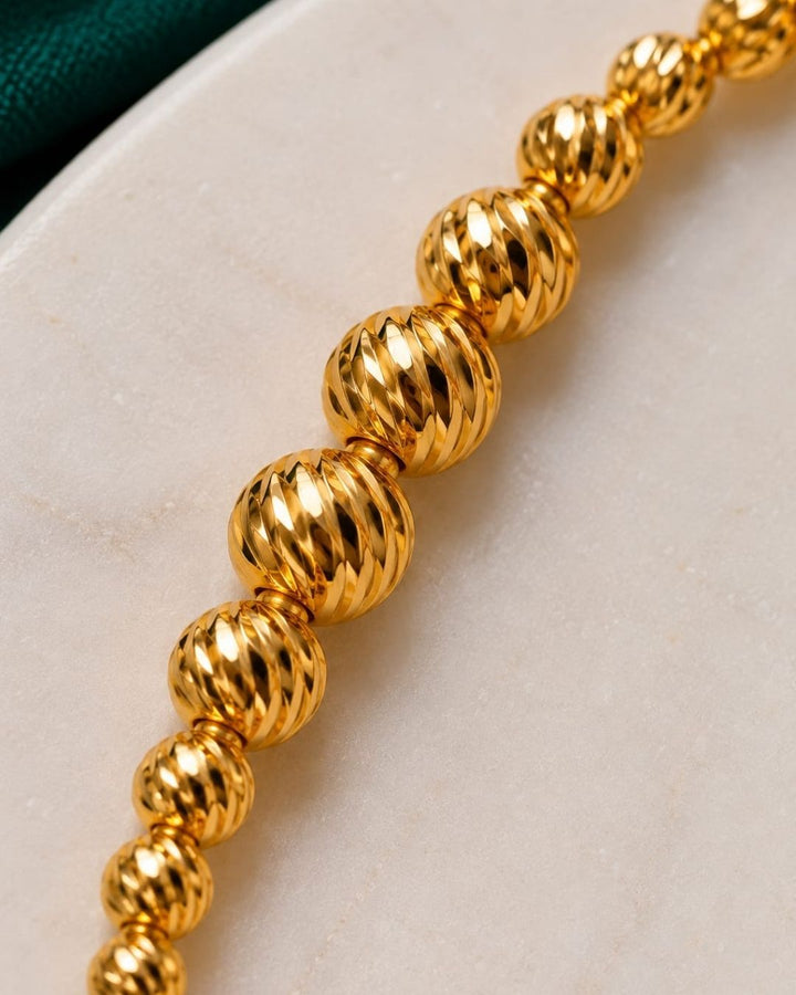 Beautiful gold plated beaded bracelet featuring a sequence of intricately textured round beads, delicate chain detailing, and a polished finish. Perfect for everyday wear, festive occasions, traditional outfits, parties, and gifting.