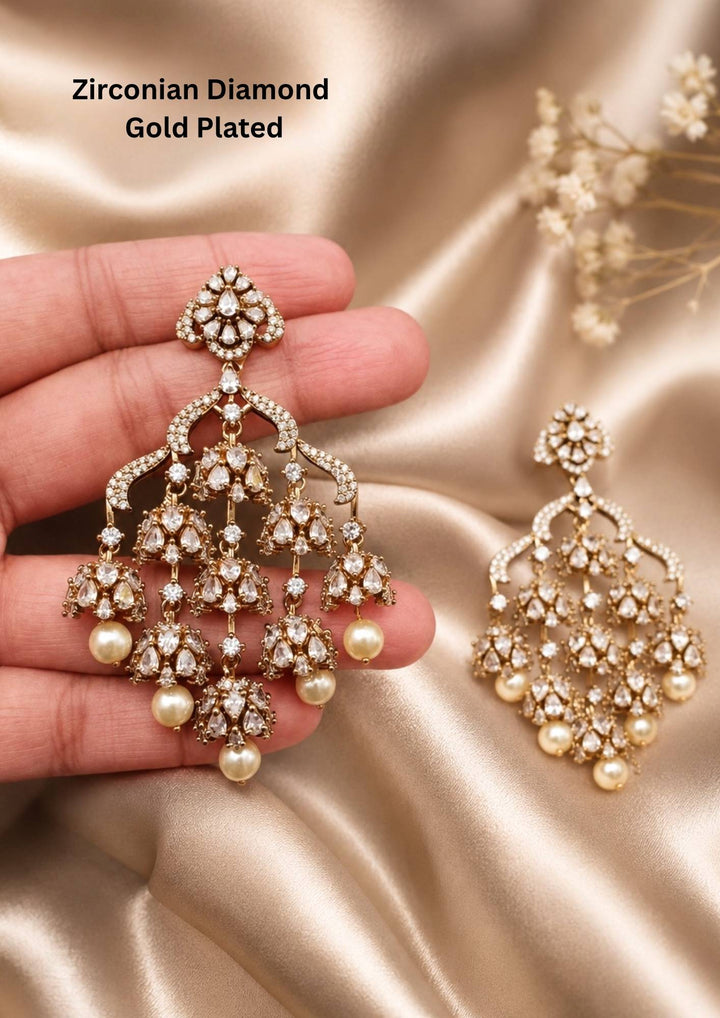 Modern Zircon Diamond gold plated heavy chandelier earrings. The design features a diamond-shaped top stud encrusted with white CZ stones, connecting to a wide arches layout. Suspended from the frame are three layers of small, delicate jhumka domes covered in sparkling American diamonds, finished with large hanging white pearls. Perfect for office, wedding, festivals