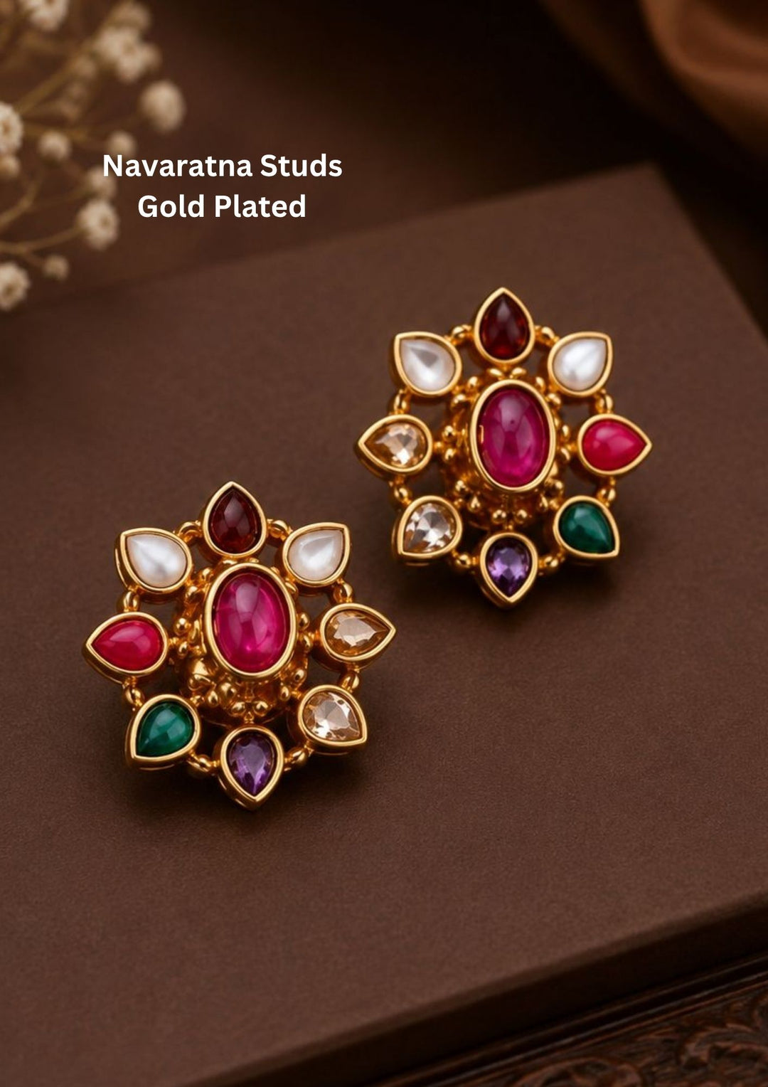 A pair of classic gold plated flower stud earrings showcasing the traditional Navaratna design with nine distinct multi-colored gemstones. The center holds a smooth oval pink ruby stone, encircled by eight tear-drop shaped petals representing pearl, coral, emerald, sapphire, and other colorful crystals. The set is crafted with a highly polished golden finish and comfortable post backings.