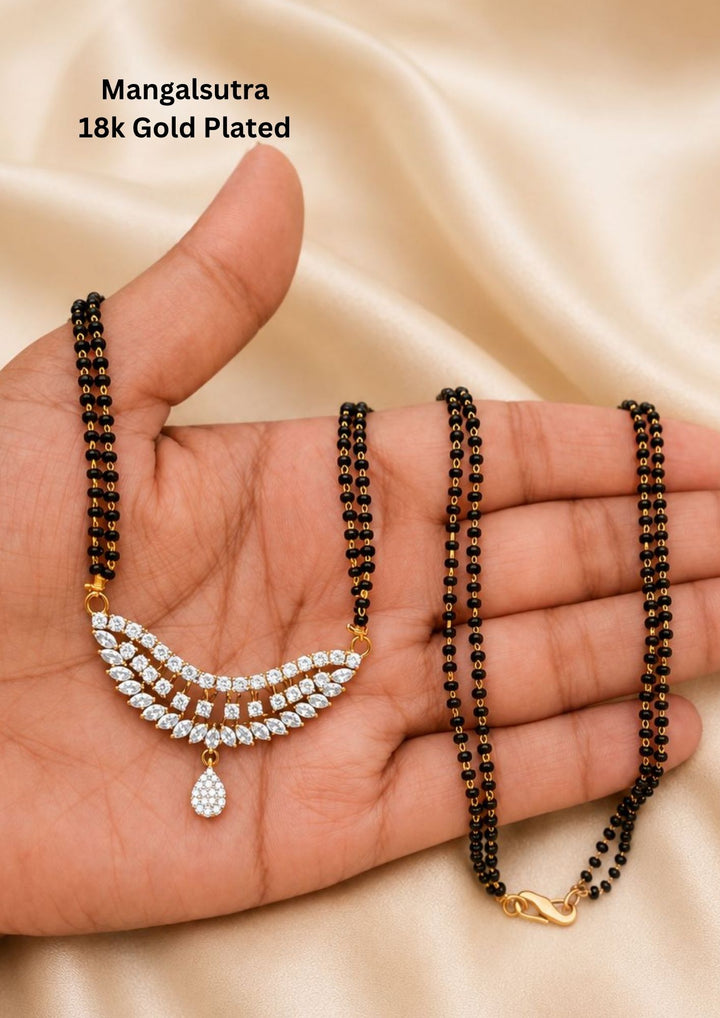 Minimalist 18k gold plated mangalsutra featuring a double strand of fine black beads holding a tiered arc pendant set with brilliant marquise-cut white zircons and a teardrop stone hanging at the center.