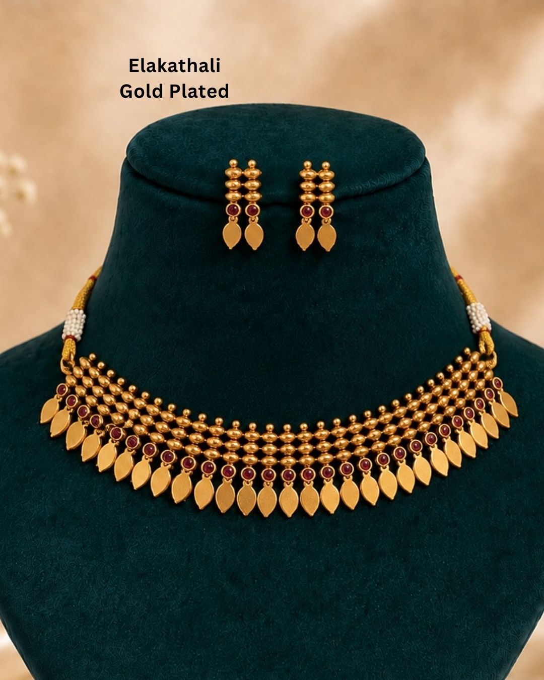 Premium gold plated Elakathaali necklace set featuring intricate traditional beadwork, red stone accents, and a row of elegant leaf-shaped motifs, paired with matching earrings. Perfect for weddings, festive occasions, traditional wear, parties, and gifting.
