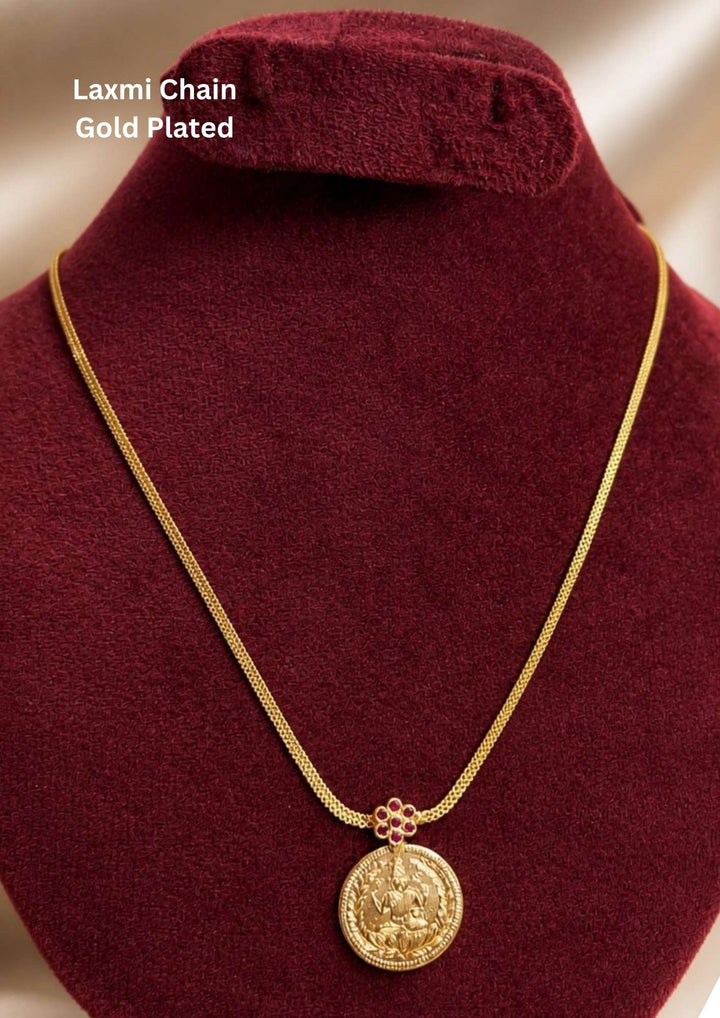 Laxmi chain gold plated traditional necklace featuring a circular coin pendant embossed with Goddess Lakshmi seated on a lotus, connected by a small pink ruby stone floral accent to a thick textured mesh chain. This classic South Indian style necklace is crafted with a premium gold finish that provides a rich divine appearance suitable for weddings, festivals, poojas, family functions, Varalakshmi Vratam, Diwali, sarees, and ethnic outfits with skin-friendly quality, anti-fade polish, comfortable fitting,