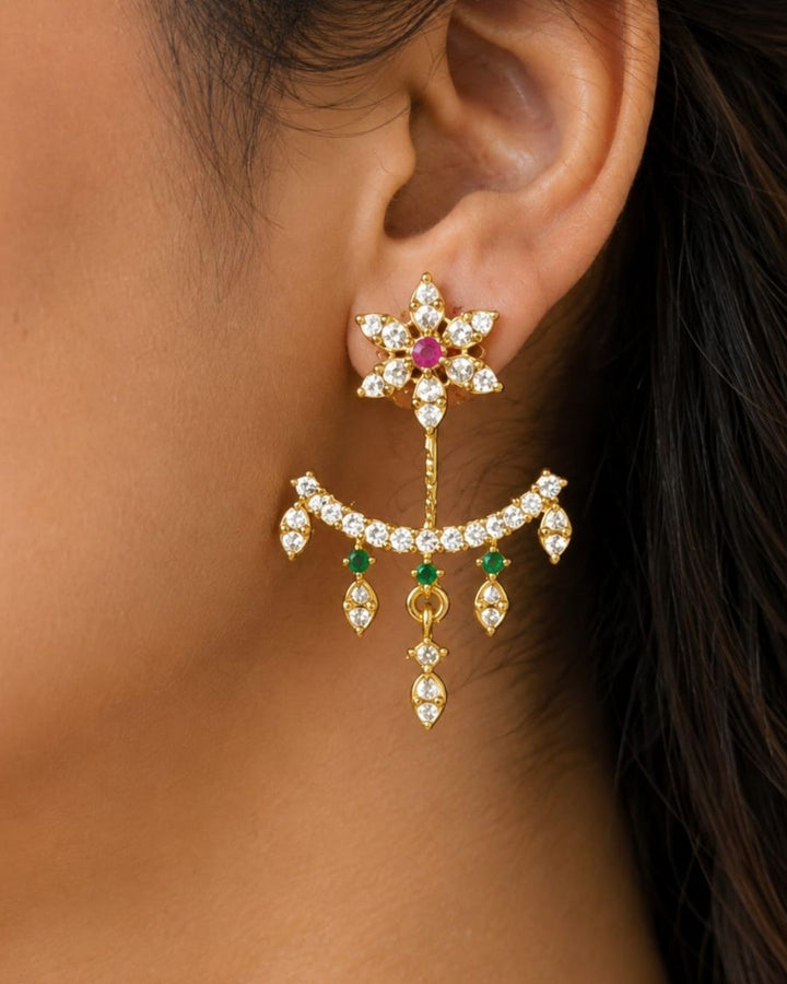 Beautiful gold plated designer dangler earrings featuring intricate floral detailing, sparkling CZ stones, pink and green accents, and delicate hanging drops. Perfect for festive occasions, parties, traditional wear, and gifting.