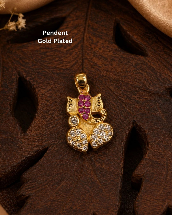 A gold-plated Ganesha pendant decorated with pink gemstones and clear stones, displayed on a dark brown carved wooden leaf with &
