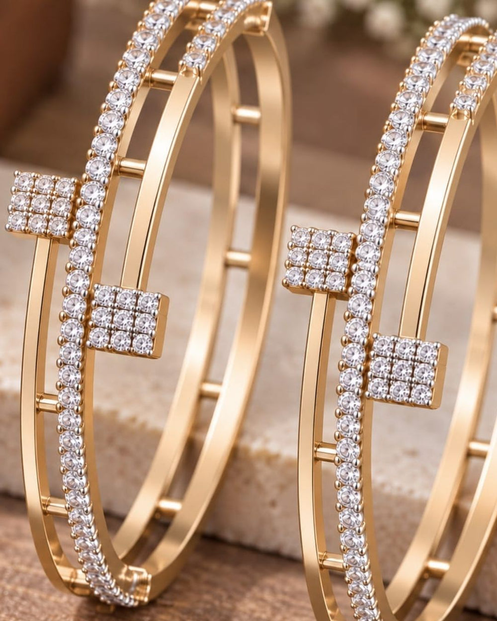 Pair of gold plated crystal bangles displayed on a navy blue jewellery box with a luxurious dark blue background.