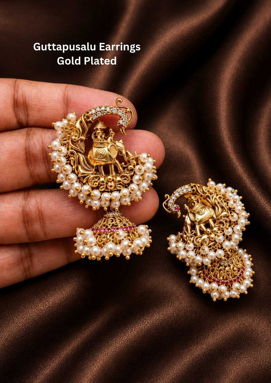 Gold plated Guttapusalu jhumka earrings designed top stud with an elephant motif. The outer curved edge of the stud is decorated with a line of small white stones and a full fringe of small white pearls. A classic dome-shaped jhumka base hangs below, highlighted by a thin row of pink ruby stones and a matching heavy cluster of hanging white pearls along the bottom rim, providing a premium heritage appearance suitable for family gatherings, festivals, parties.