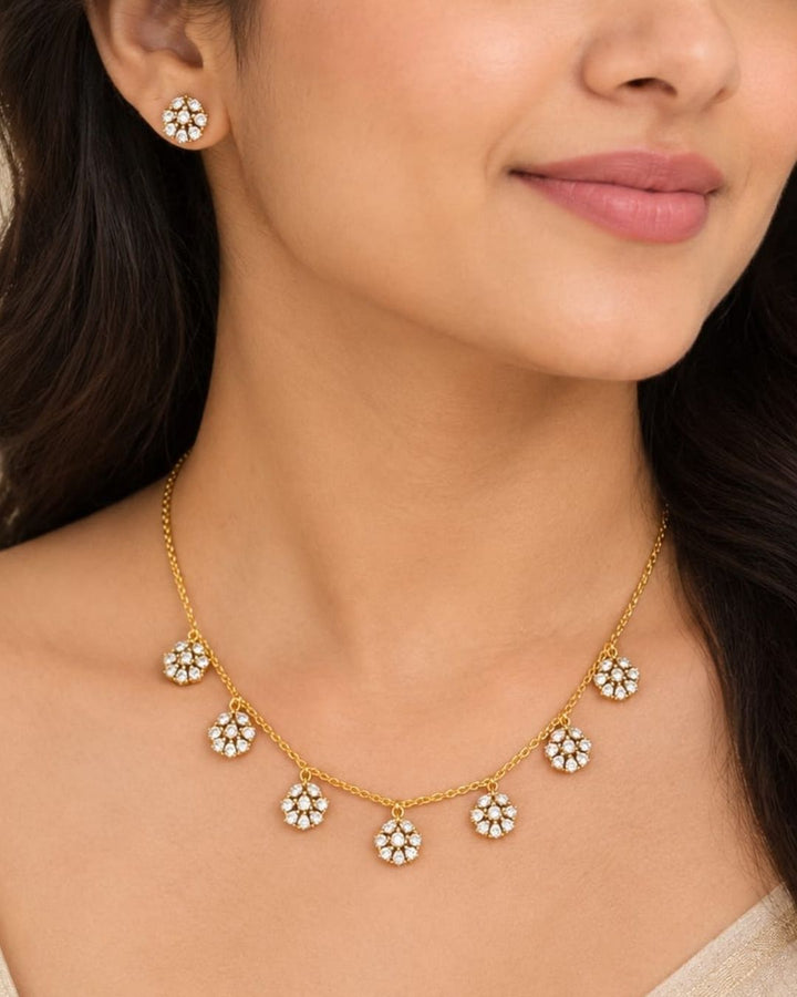 Elegant gold plated necklace with sparkling white zircon stones and floral dangling motifs displayed on a navy blue jewellery bust.