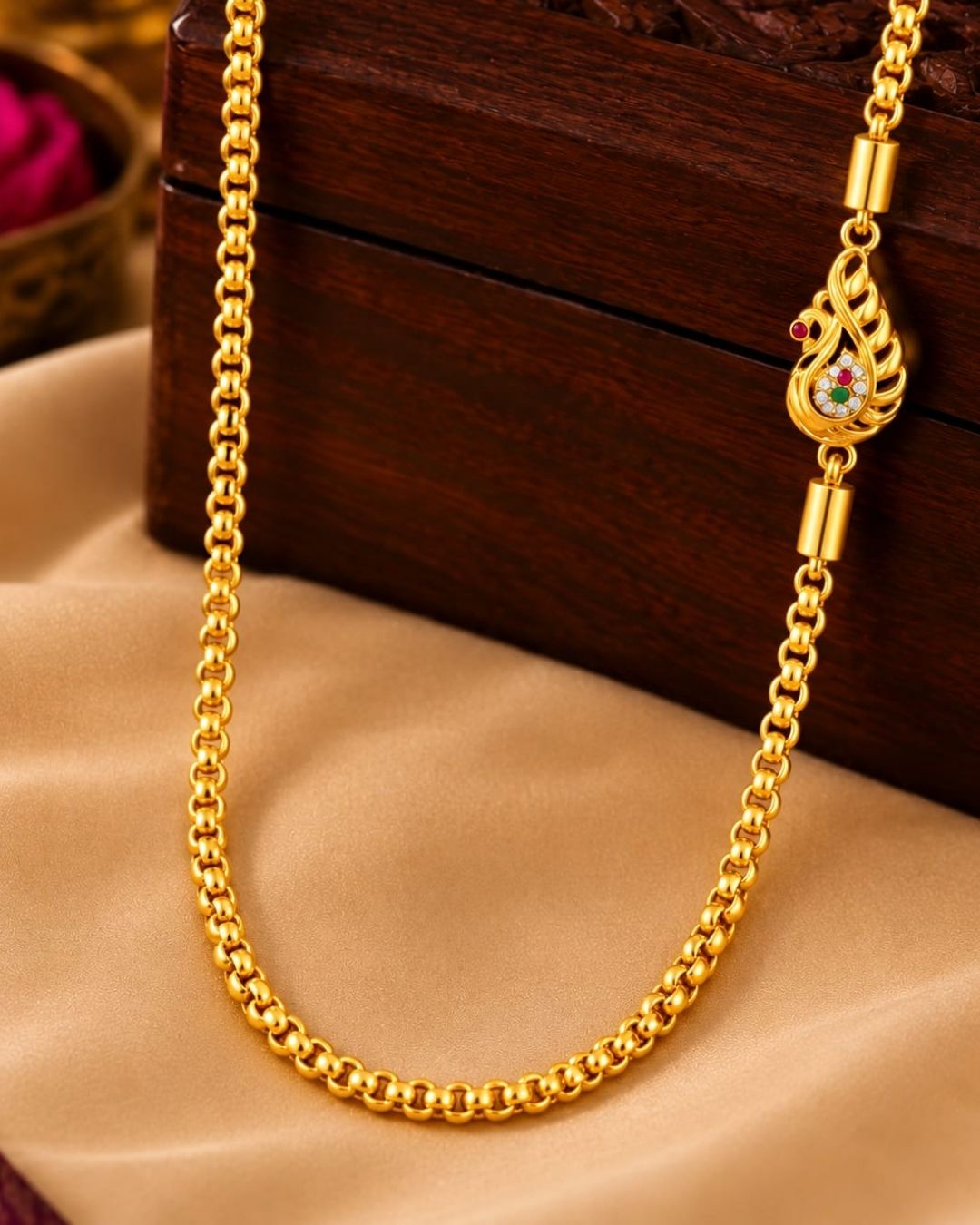 Elegant gold plated thalli chain displayed on beige silk with a carved wooden jewellery box, featuring a simple chain and a detailed ornamental clasp.
