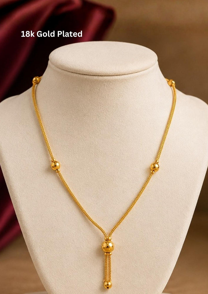 A sleek and minimalist 18k gold plated festive chain necklace featuring a delicate woven rope link. The chain is interspersed with small, polished gold spheres that guide the eye down to a central Y-shaped drop accent, complete with a larger hanging metallic globe bead, perfect for functions, weddings