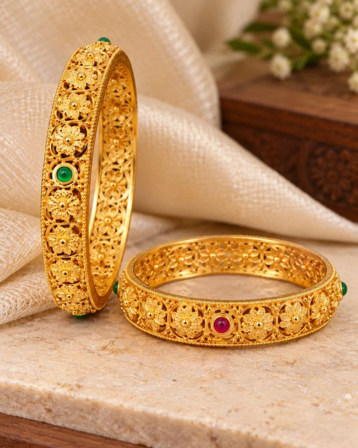 Elegant 18K gold plated floral bangles displayed on a carved wooden jewellery box, showcasing ornate gold craftsmanship and green and ruby stone details.