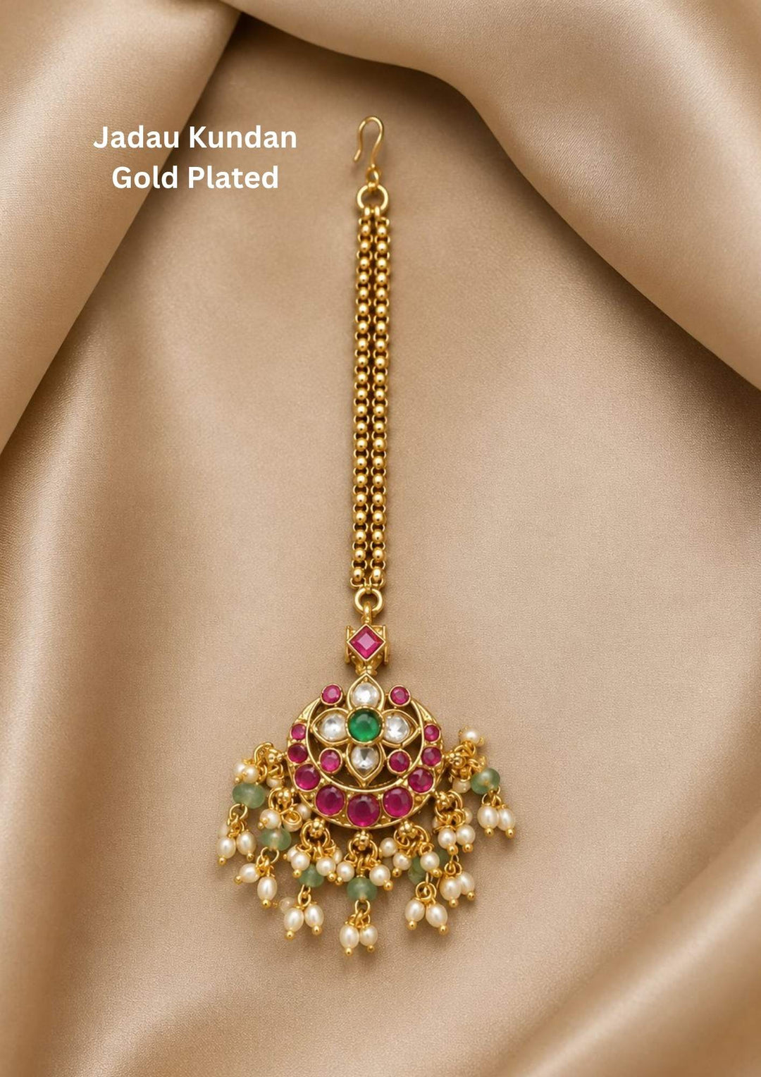 Jadau kundan gold plated circular maang tikka featuring a crescent floral pattern set with ruby pink stones, an emerald green center, white kundan accents, and hanging white pearls with light green quartz beads. This lightweight tikka is crafted with a double-beaded chain strand and a secure top hook providing a rich and classy appearance suitable for weddings, festivals, receptions, poojas, family functions with skin friendly quality, anti fade polish, comfortable fitting.