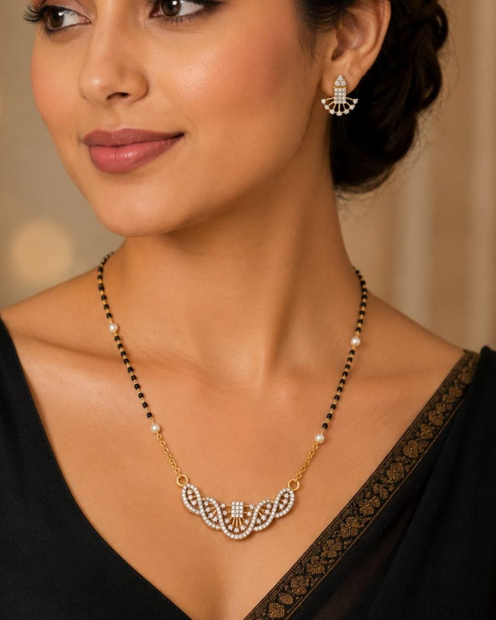 A woman wearing a gold and black beaded necklace with a white stone pendant, matching drop earrings, and a black sari with gold embroidery.
