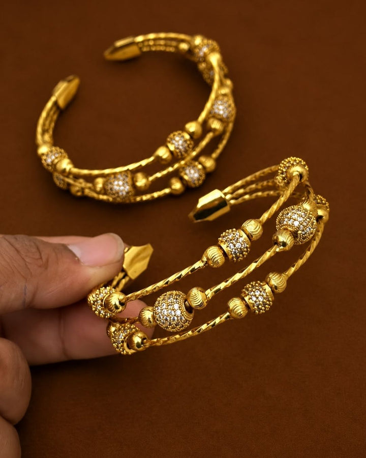 Gold plated adjustable kada for women featuring a triple twisted design, decorative gold beads, and sparkling white stone embellishments.