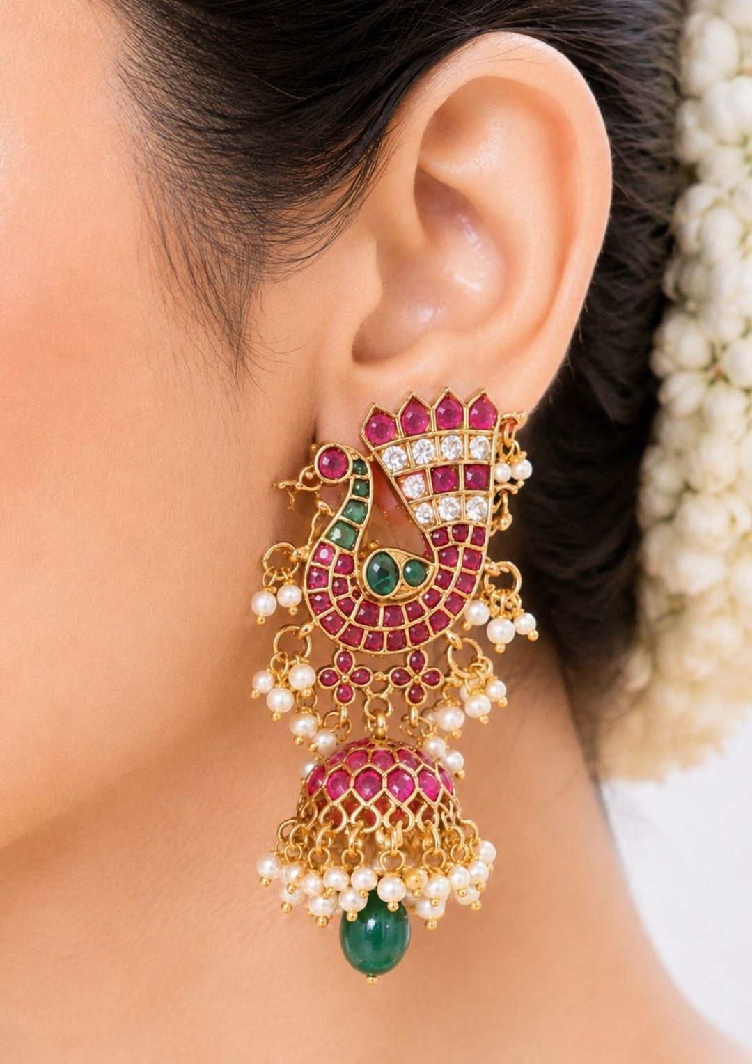 South Indian women wearing gold plated Jadau kundan jhumka earrings designed with an elegant pink ruby peacock pattern, shimmering kundan stone accents, and delicate pearl drop clusters that give a graceful traditional royal look for weddings, festive occasions, and temple visits with lightweight comfortable use