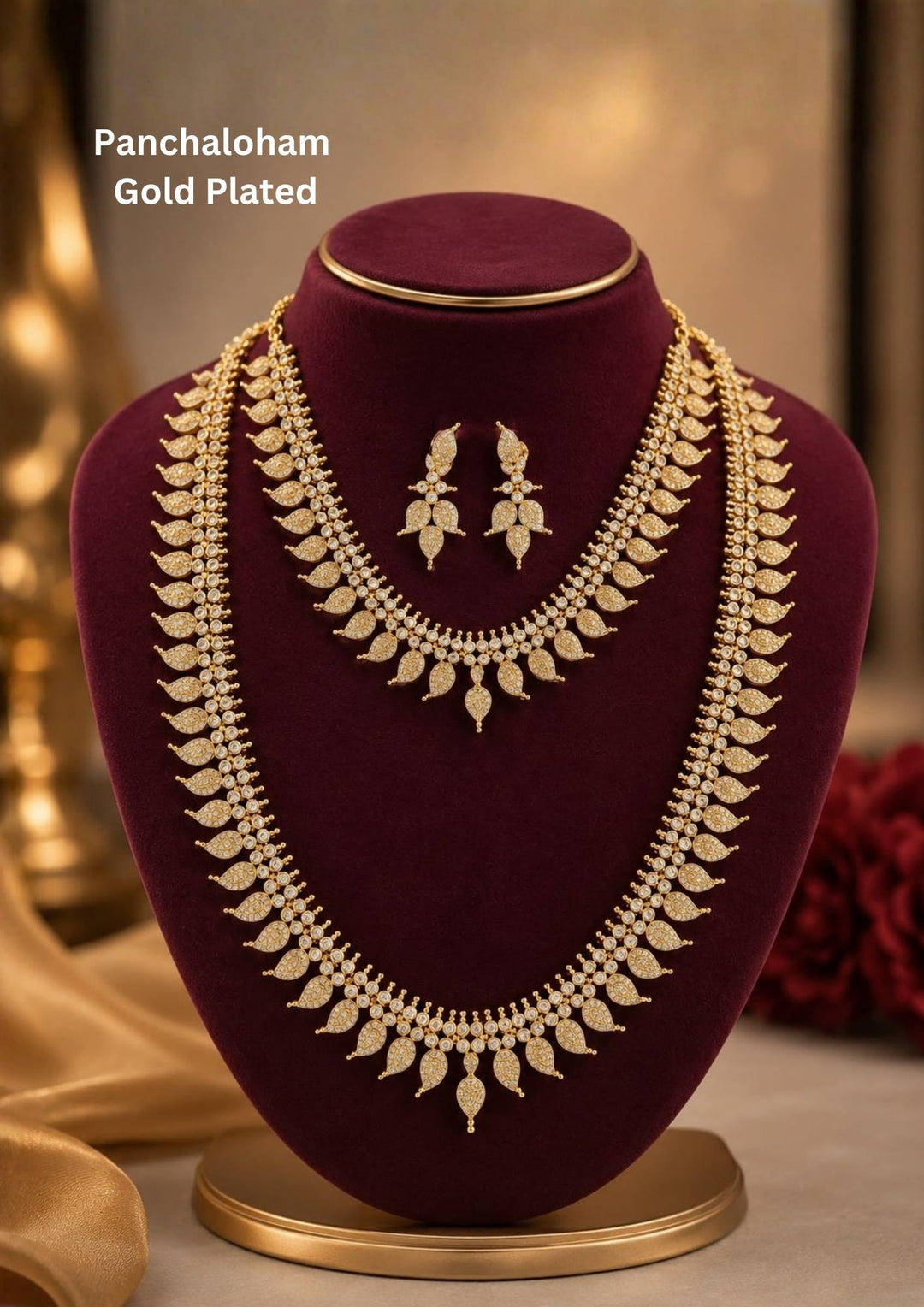 Traditional Panchaloham gold plated bridal combo set featuring a short choker necklace and a matching long haram chain, both intricately designed with repeating mango leaf motifs densely studded with shimmering white stones. The collection is beautifully paired with matching delicate leaf drop earrings that complete the uniform elegant look and skin-friendly 