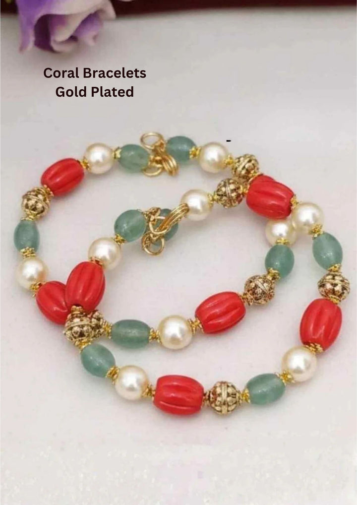 A vibrant multi-gemstone strand bracelet featuring large, oval-shaped fluted red coral beads. The coral elements alternate uniformly with smooth cream-white cultured pearls, tumbled pale green jade stones, and intricate 18k gold plated textured filigree spacer beads, all secured by a golden ring hook clasp.