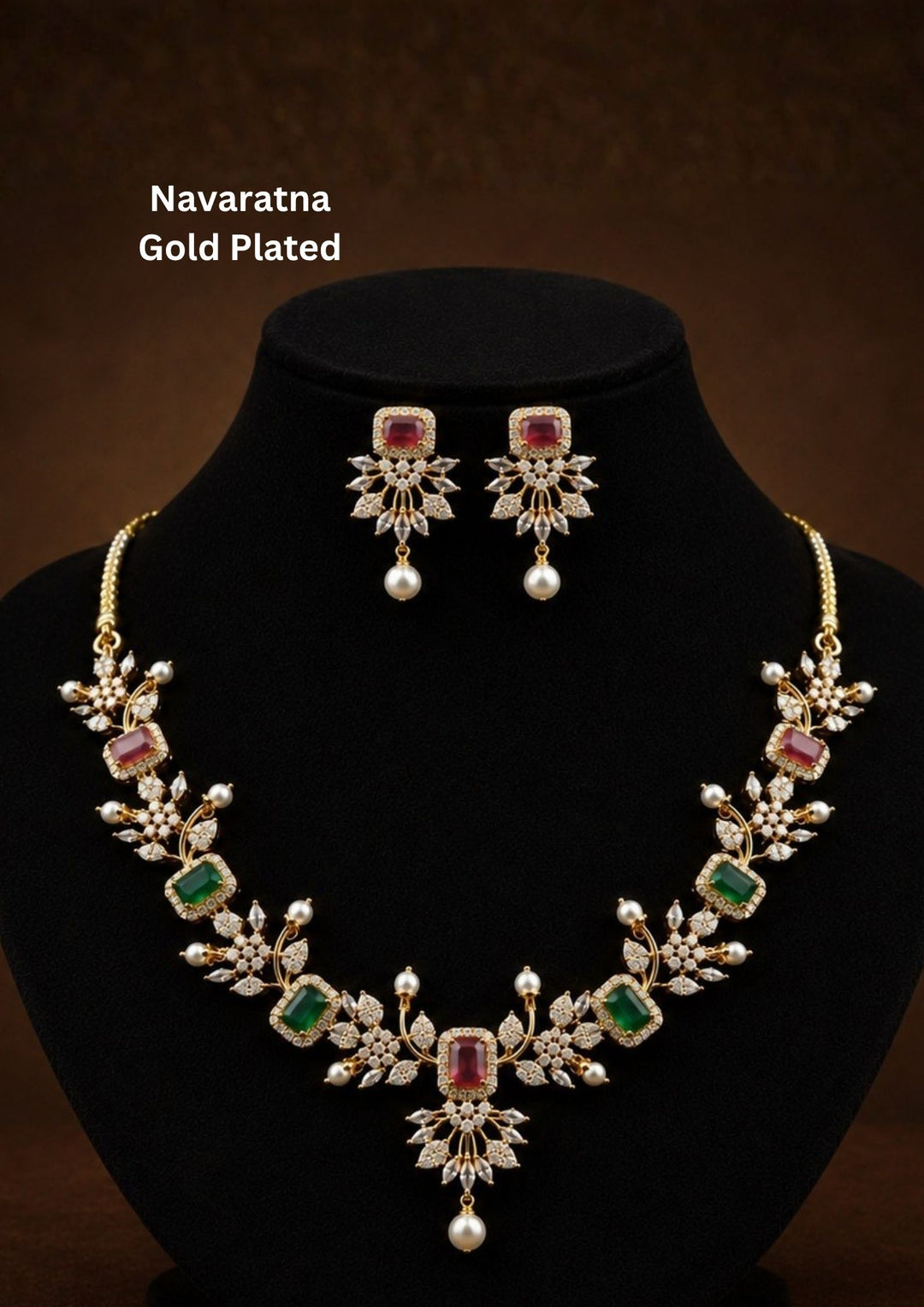 Gold-plated Navratna jewelry set featuring a necklace and matching earrings The set is adorned with gold-plated floral motifs, green rectangular stones, pink rectangular stones, and white pearl-like drops. Elegant Navaratna gold plated necklace set featuring colorful gemstone-inspired stones, pearl drops, and matching earrings for festive occasions.