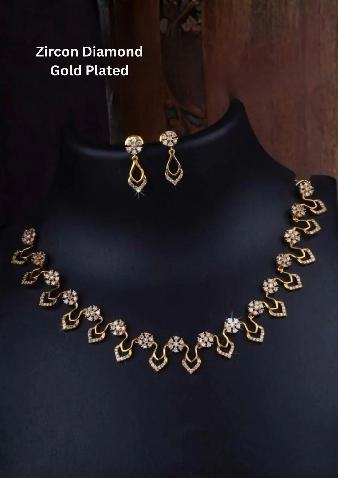 An elegant 18K gold-plated necklace set displayed on a black mannequin stand, featuring small floral clusters made of pure white zircon diamonds. The necklace has a beautiful wavy pattern with delicate, sparkly teardrop shapes hanging at the bottom. The matching drop earrings feature a matching circular diamond stud that holds a dainty, diamond-lined teardrop loop, creating a very bright and luxurious appearance.