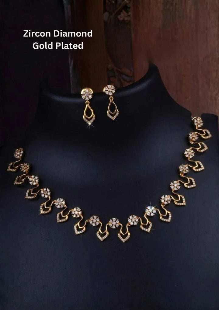 An elegant 18K gold-plated necklace set displayed on a black mannequin stand, featuring small floral clusters made of pure white zircon diamonds. The necklace has a beautiful wavy pattern with delicate, sparkly teardrop shapes hanging at the bottom. The matching drop earrings feature a matching circular diamond stud that holds a dainty, diamond-lined teardrop loop, creating a very bright and luxurious appearance.