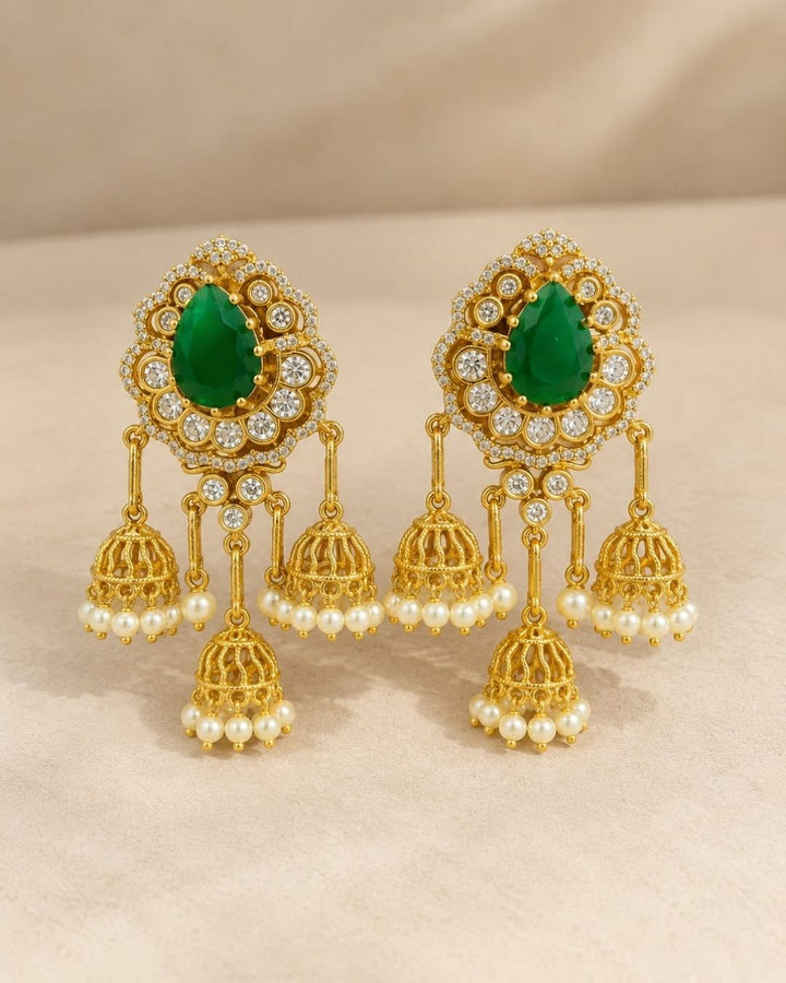 Gold plated zircon diamond jhumka earrings featuring ruby red teardrop stones, clear sparkling stones, and multiple pearl-decorated gold jhumka hangings.