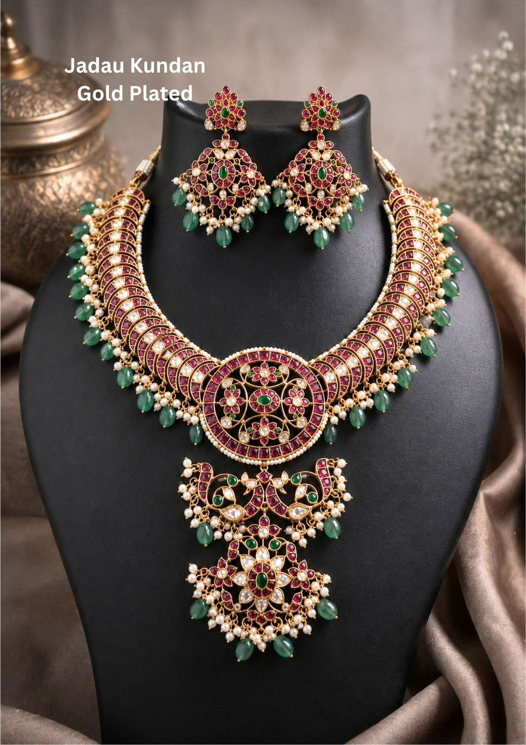 Gold plated Jadau Kundan jewelry set in image_e6bd29.png featuring a broad, curved collar choker necklace meticulously detailed with red kemp-style fills and tiny pearl borders. The center showcases a large circular medallion connected to a multi-tiered dangling floral pendant. The entire lower fringe of the necklace is accented with soft green bead tumbles and delicate pearl clusters. Includes a matching pair of heavy, diamond-shaped hanging earrings. Perfect for weddings and festivals