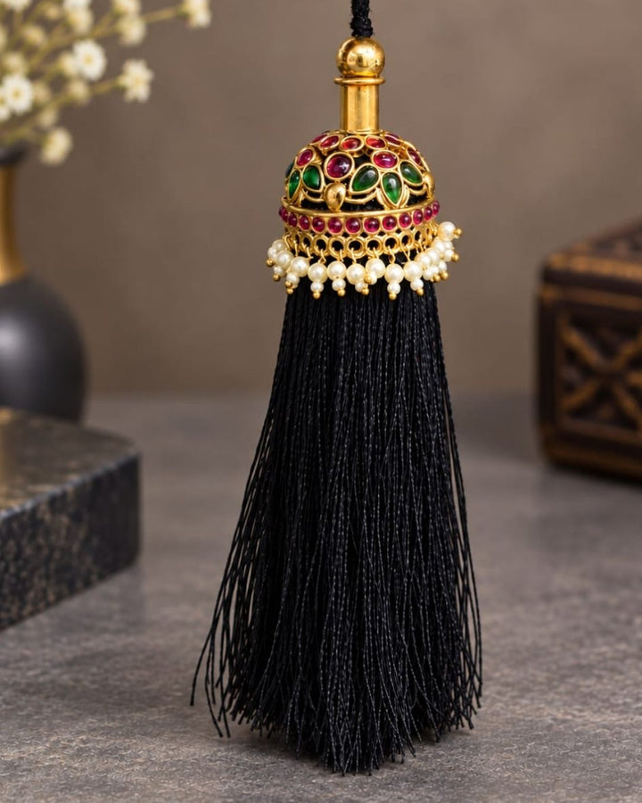 Elegant gold plated Jada Gantalu with intricate dome-shaped detailing, green and ruby stones, pearl accents, and long black thread tassels, perfect for bridal and festive hairstyles.