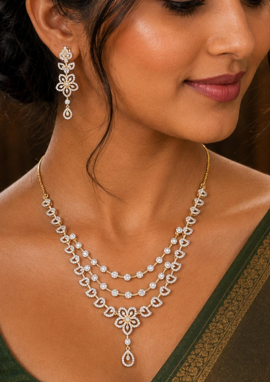 South Indian Women wearing a Elegant zircon diamond gold plated jewelry set featuring a triple-layered necklace and matching drop earrings. The set showcases intricate floral and leaf-inspired motifs studded with sparkling white zircon stones, ending in a delicate teardrop dangle against a deep blue display bust.