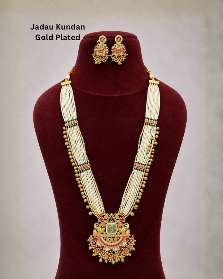 Traditional gold plated necklace set with layered white bead strands, green and pink stone accents, an elaborate pendant with dangling beads, and matching earrings, perfect for festive and ethnic occasions.