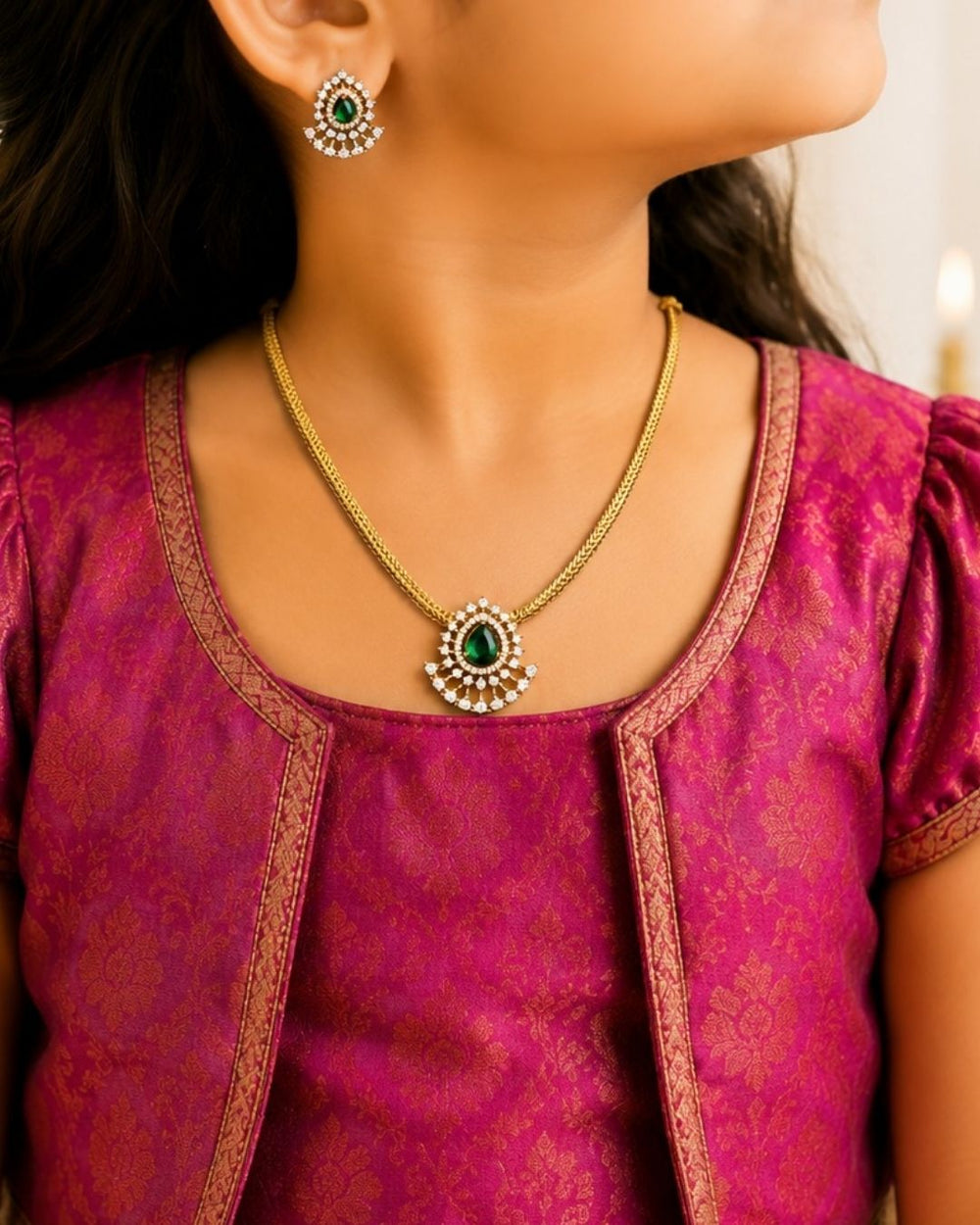 A minimalist 18k gold plated herringbone chain necklace featuring a central teardrop-shaped ruby green stone. The stone is enclosed in a halo of white pure Zircon diamonds that flares out at the bottom into a shimmering, fan-shaped scalloped fringe, paired with matching crown-set ear studs.