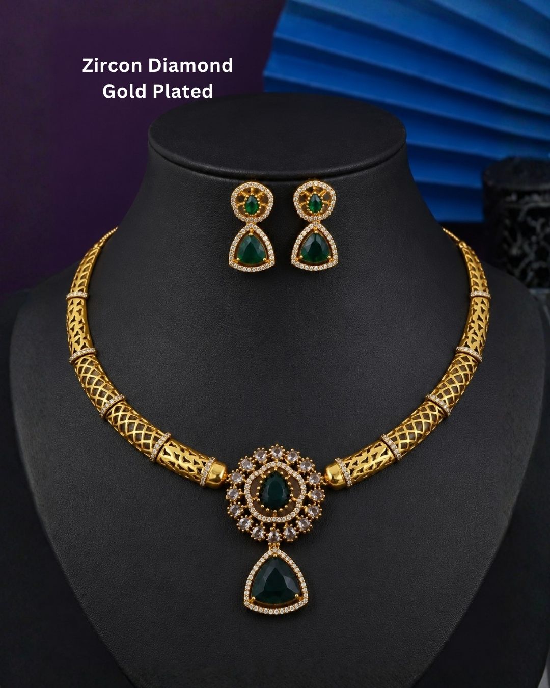 Gold-plated necklace and matching earrings set displayed on a black jewelry bust. The necklace features a textured gold chain with a central teardrop pendant and matching drop earrings, embellished with green stones and small clear stones.