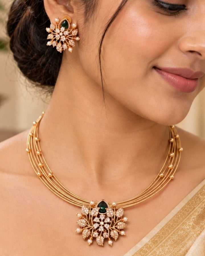 zircon diamond gold plated necklace with earrings designed with white pearls and leaf shaped gold beads with green emerald stone in middle. This necklace set has a premium gold finish, is lightweight, and comfortable to wear. Suitable for daily use, pooja, weddings, festivals, functions, and family occasions. It is sweat-proof, anti-fade, skin-friendly, and easy to wear daily