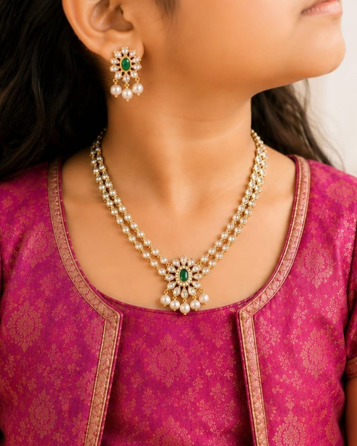 Zircon diamond gold plated two-layer necklace set featuring double rows of shimmering teardrop white zircon stones, an elegant central floral accent with an oval green emerald, and delicate hanging white pearls. This matching lightweight set includes floral emerald drop earrings with pearl details, providing a rich, royal appearance suitable for weddings, re-marriages, festivals, receptions, family functions, sarees, lehengas, and ethnic outfits with skin-friendly quality, anti-fade polish, comfortable fit.