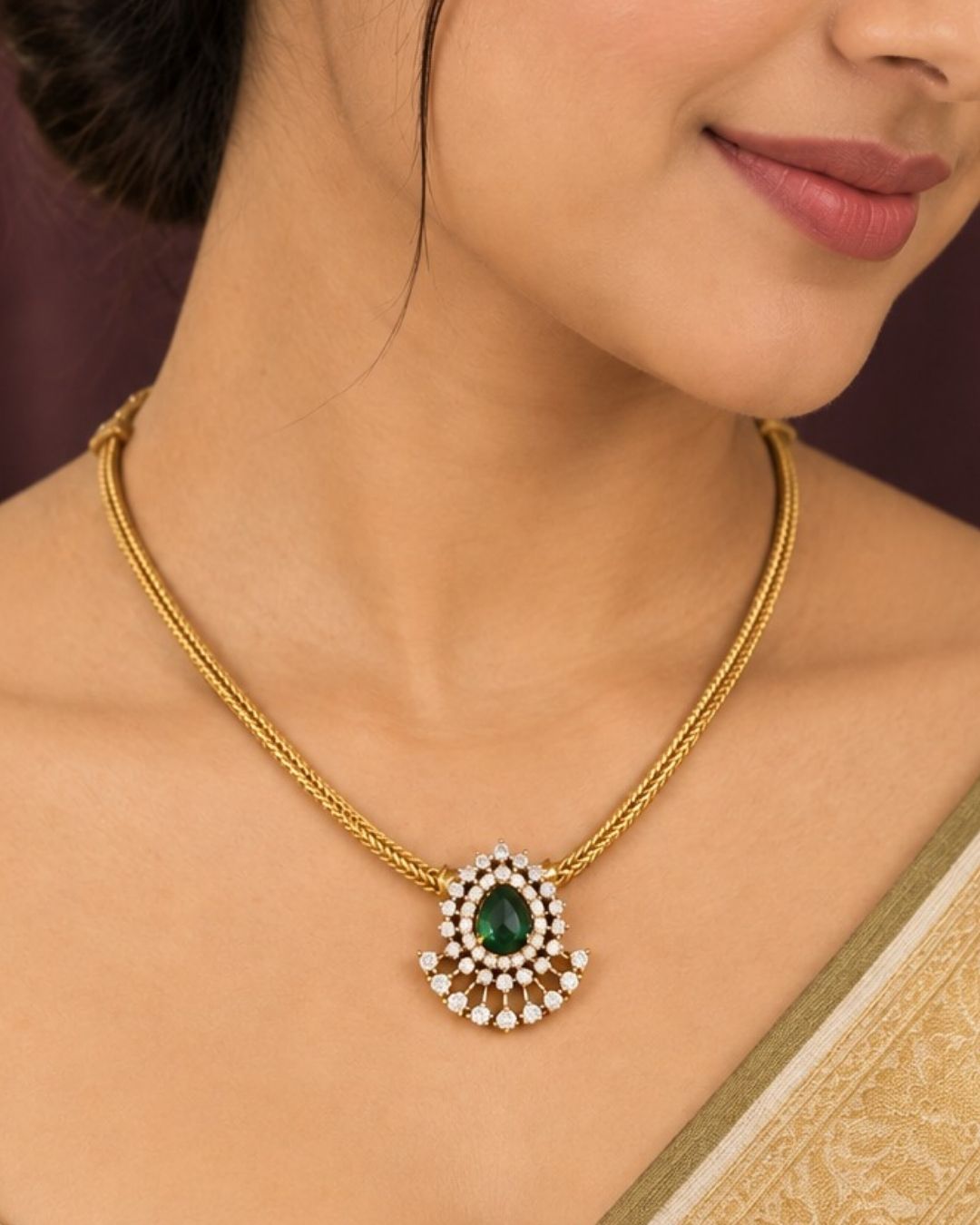 A minimalist 18k gold plated herringbone chain necklace featuring a central teardrop-shaped ruby green stone. The stone is enclosed in a halo of white pure Zircon diamonds that flares out at the bottom into a shimmering, fan-shaped scalloped fringe, paired with matching crown-set ear studs.