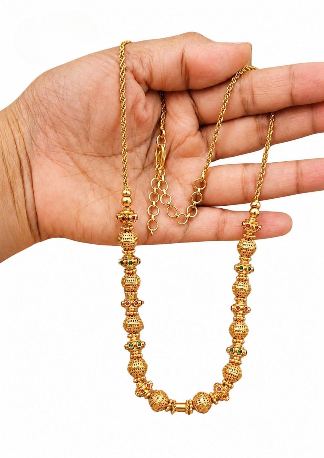 Gold plated long chain haraam necklace featuring elegant textured golden spheres alternating with small spacer rings inset with red ruby and green emerald stone accents. This lightweight chain is crafted with a detailed twisted rope style chain extension held in hand to provide a classy and premium appearance suitable for daily wear, office wear, casual outings, family gatherings, festivals, parties and traditional occasions with skin friendly quality, anti fade polish, comfortable fitting