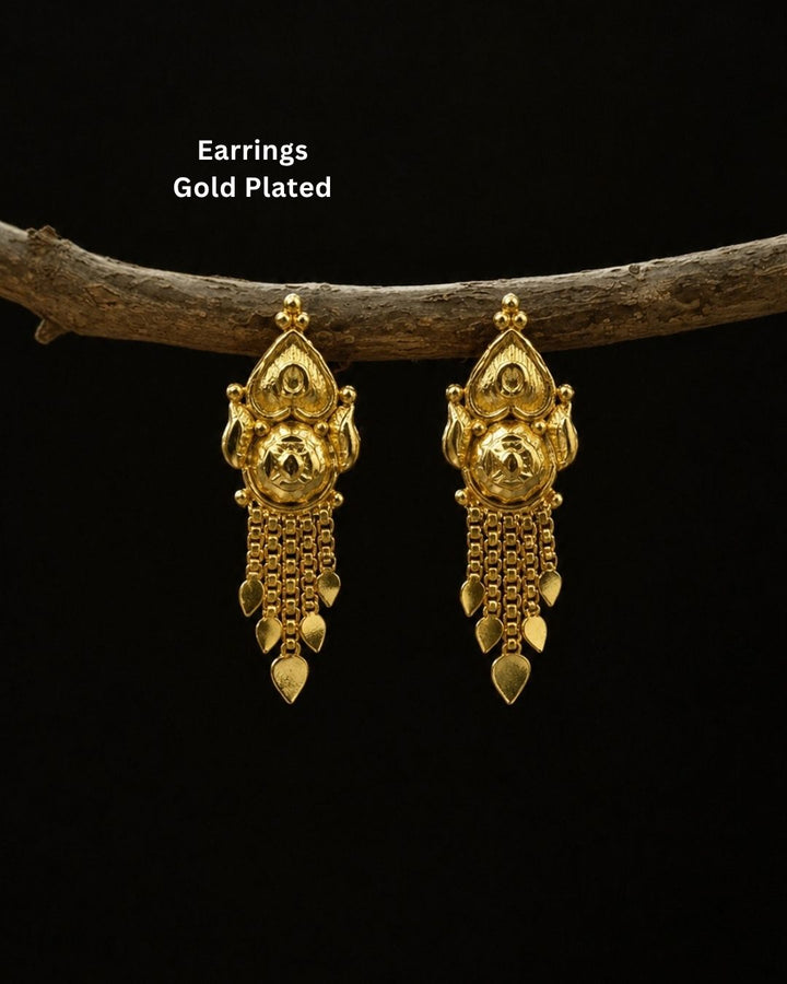 A pair of gold-plated traditional Indian jhumka earrings hanging from a rustic wooden branch against a solid black background, with white text overlay reading &