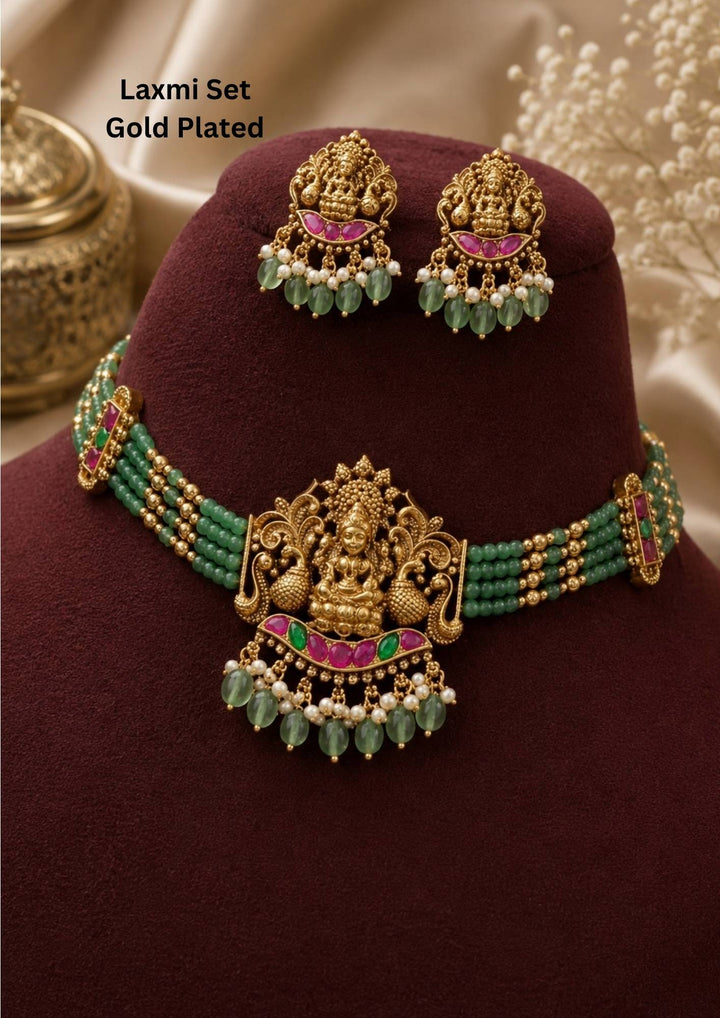 Jadau kundan 18K gold plated temple choker necklace set featuring Goddess Lakshmi motif, green bead strings, pink and green kundan stones, pearl hangings and antique temple jewellery finish with matching earrings. This traditional South Indian jewellery set gives a rich bridal and festive appearance suitable for weddings, poojas, festivals, Bharatanatyam, sarees, lehengas and ethnic outfits with lightweight comfortable fitting, anti fade polish and Cash on Delivery available now.
