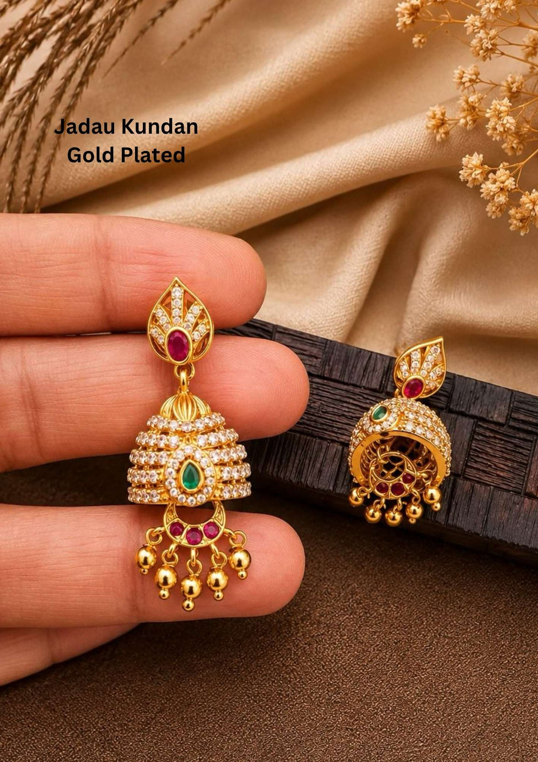 gold plated brass base jhumka earrings featuring a leaf-shaped top stud with a pink ruby stone, a classic dome base wrapped in shimmering white zircon diamond rows with a central green stone teardrop, and dangling gold bead drops. Perfect for weddings, festivals, and parties with skin-friendly premium quality, comfortable lightweight fitting, and Cash on Delivery available now.