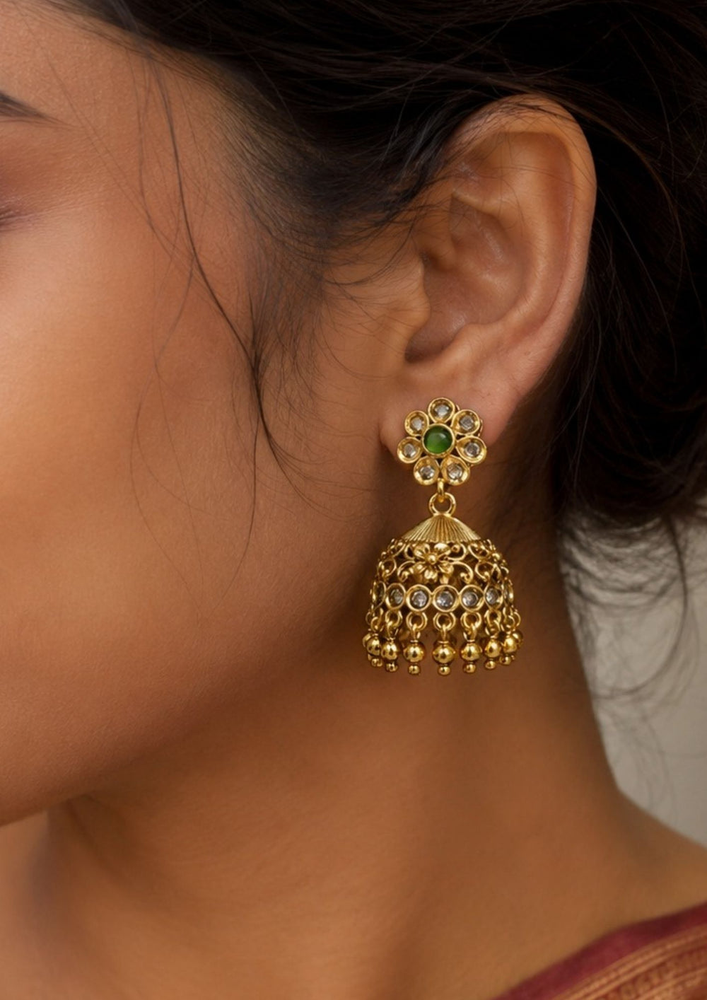 South Indian woman styling emerald beads gold plated jhumka earrings with traditional attire. The earrings feature floral motifs, antique gold finish and classic hanging bead detailing perfect for sarees, lehengas and festive occasions.