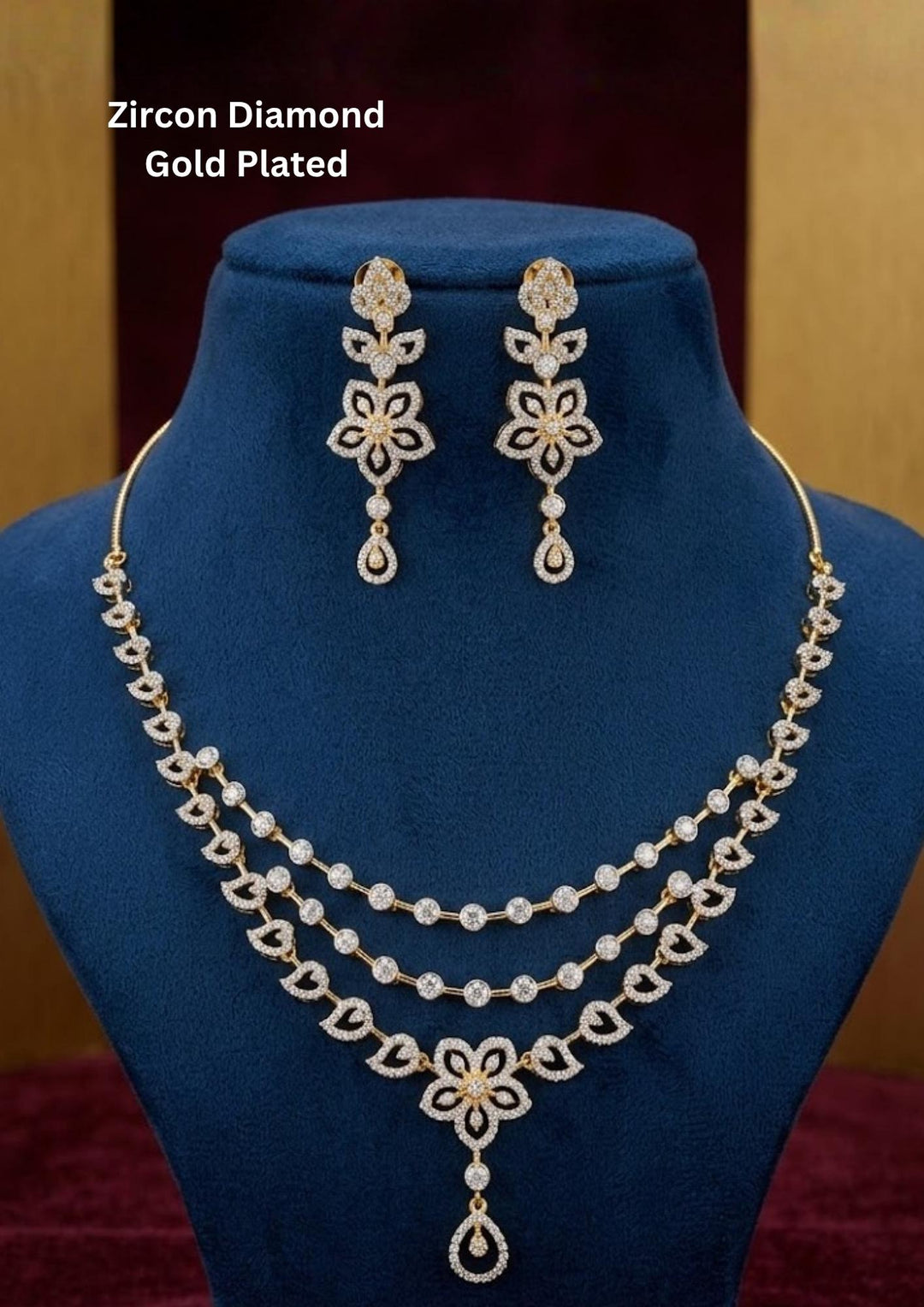 Elegant zircon diamond gold plated jewelry set featuring a triple-layered necklace and matching drop earrings. The set showcases intricate floral and leaf-inspired motifs studded with sparkling white zircon stones, ending in a delicate teardrop dangle against a deep blue display bust.