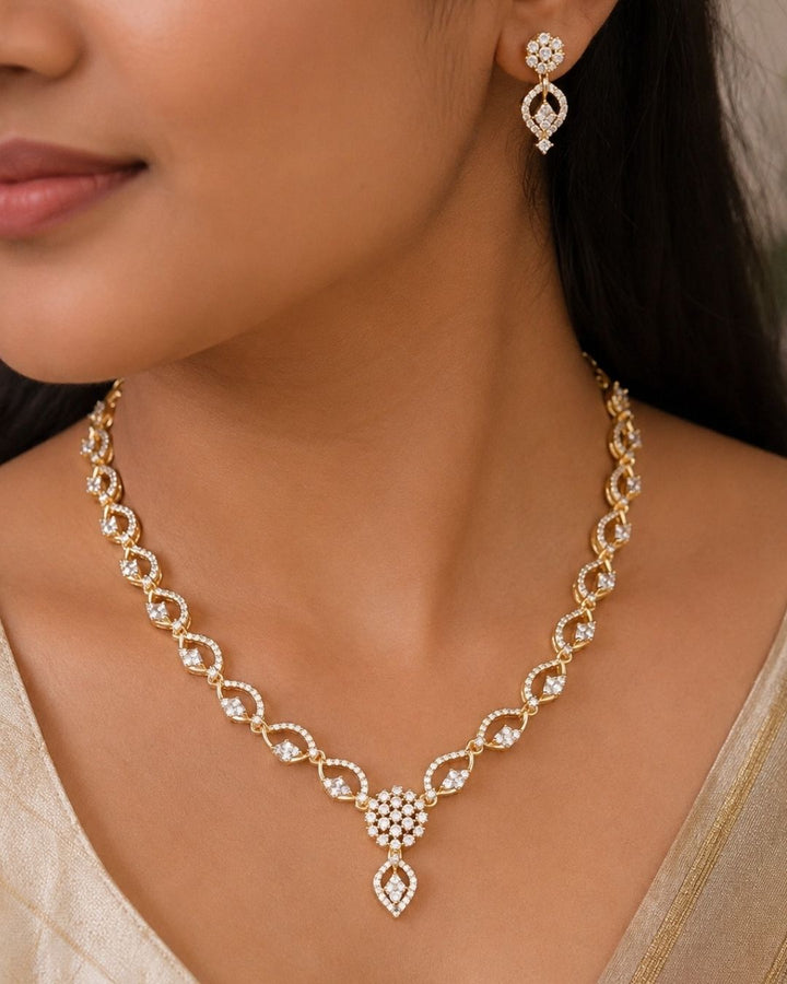 Beautiful gold plated necklace set featuring repeating loop-shaped links embellished with sparkling stones, a floral-inspired pendant, and matching drop earrings. Perfect for traditional wear, festive occasions, weddings, parties, and gifting.