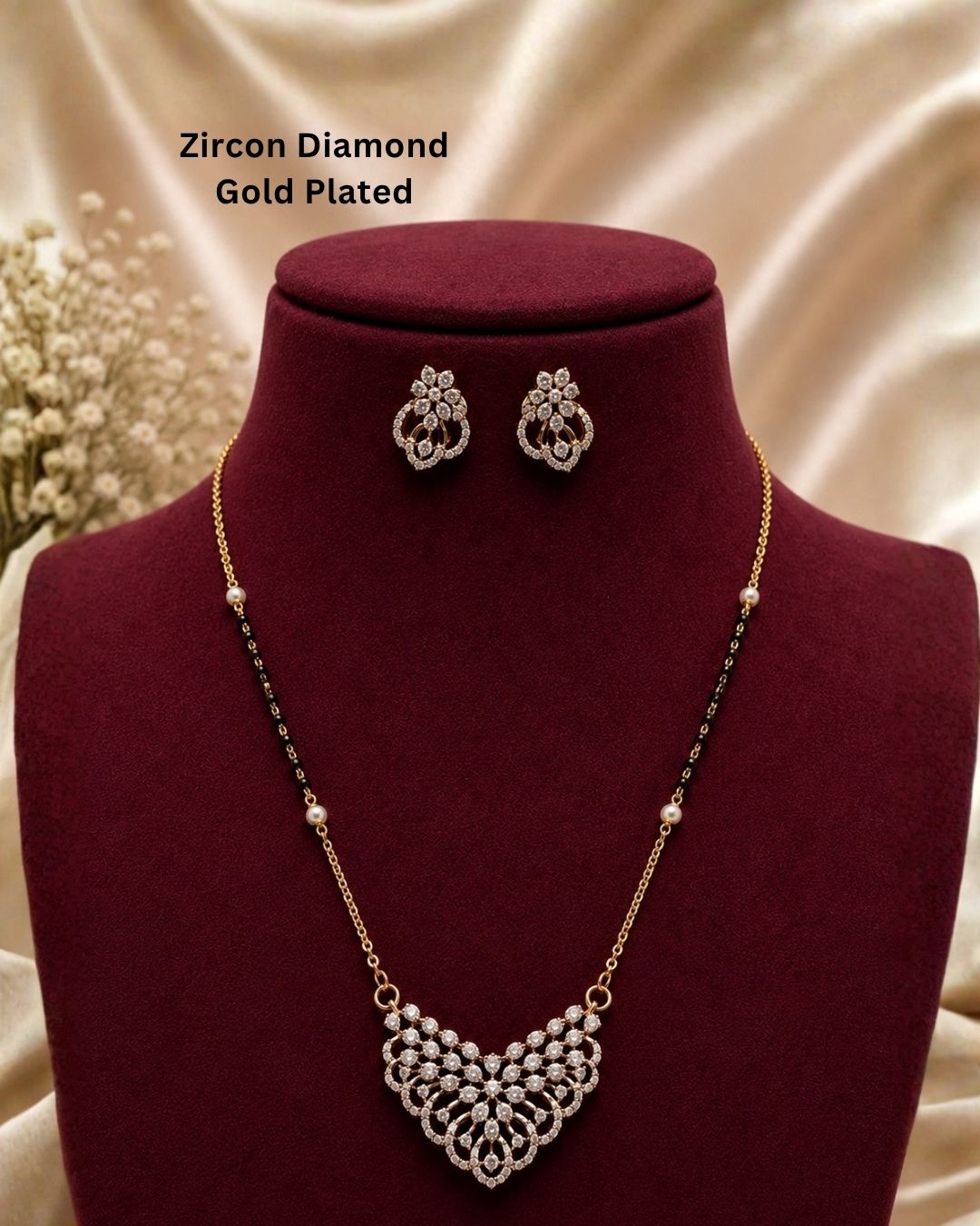 Gold-plated zircon necklace and matching stud earrings displayed on a dark red velvet jewelry bust. The necklace features a detailed gold-plated pendant with clear zircon stones and a beaded chain with alternating gold and black beads.
