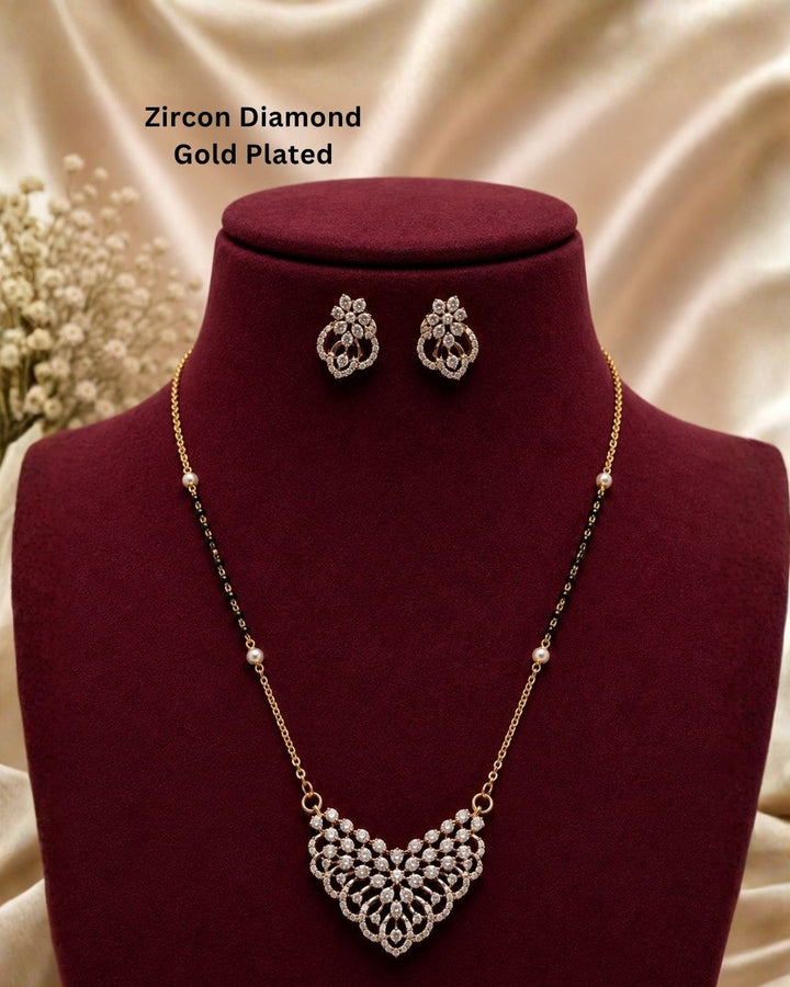 Gold-plated zircon necklace and matching stud earrings displayed on a dark red velvet jewelry bust. The necklace features a detailed gold-plated pendant with clear zircon stones and a beaded chain with alternating gold and black beads.
